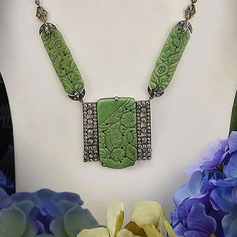 Um eine Juweliers-Büste hängt ein Collier aus Jade im typischen Art Deco Look. Darum herum sind blaue Blüten als Dekoration